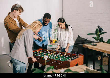 Unternehmerinnen Spielen Tischfußball und zwei männlichen Kollegen zeigen an Bord Spiel Stockfoto