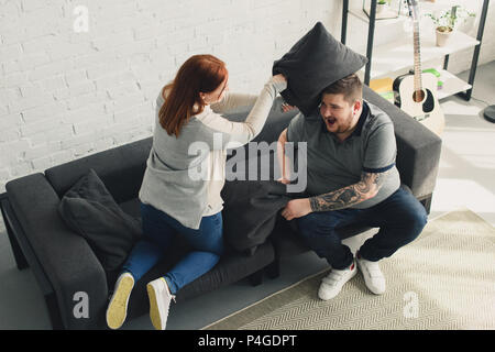 Freund und Freundin kämpfen mit Kissen auf dem Sofa zu Hause Stockfoto