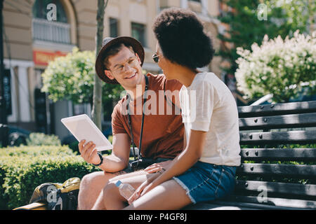 Interracial Paar Touristen sitzt auf der Bank mit digitalen Tablet Stockfoto