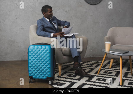 Im mittleren Alter Geschäftsmann sitzen und lesen Zeitung und gleichzeitig auf Watch Stockfoto