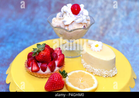 Feder Desserts auf einem gelben stehen, Eisbecher, Erdbeer und Zitrone Custard tart, glasierten Kuchen mit weißer Schokolade curl, alle individuellen Größe Stockfoto