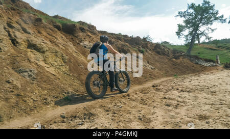 Fat bike auch fatbike oder Fat Tire Bike Im Sommer fahren auf der Straße. Der Kerl Fahrten durch die Hügel, der auf einem sand Ton weg, hinter ihm die Ufer durch. Stockfoto