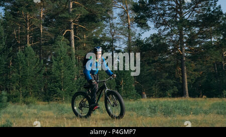 Fat bike auch fatbike oder Fat Tire Bike im Sommer Reiten im Wald. Der Kerl fährt Fahrrad zwischen Bäumen und Stümpfe. Er überwindet einige obstac Stockfoto