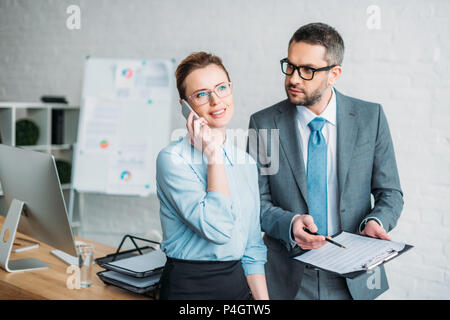 Geschäftsmann bitten, seine Kollegin Papiere zu unterzeichnen, während Sie am Telefon sprechen und ihm lästige Stockfoto