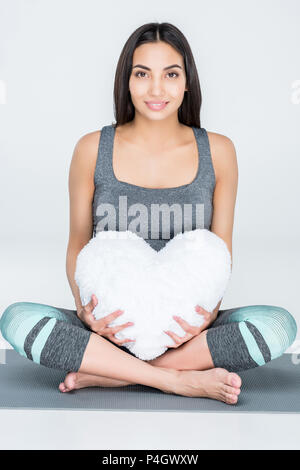 Attraktiven asiatischen schwangere Frau in Sportkleidung Holding herzförmige Kissen, isoliert auf Grau Stockfoto