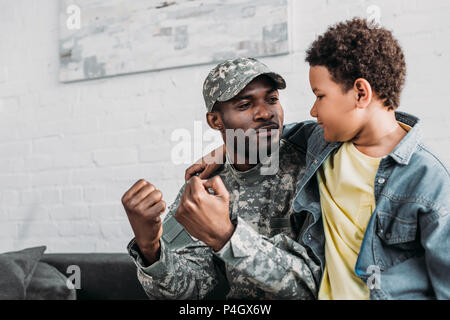 Vater in Uniform und afrikanischen amerikanischen Jungen umarmen und sprechen zu Hause Stockfoto