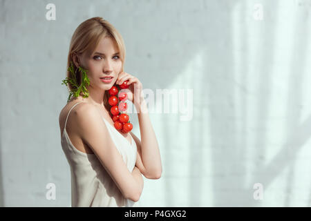 Junge Frau mit Cherry Tomaten in der Hand und Ohrring aus frischen Rucola, vegane Lebensweise Konzept Stockfoto