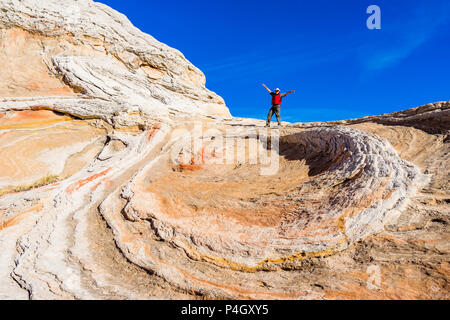 Mann, der gegen den blauen Himmel steht, mit ausgestreckten Armen über der Sandsteinvortex-Formation White Pocket Area Vermilion Cliffs National Monument, Arizona Stockfoto