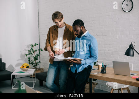 Geschäftsmann mit Papier Tasse Kaffee beobachten auf Lehrbuch und Reden der amerikanischen Kollegen zu afrikanischen Stockfoto