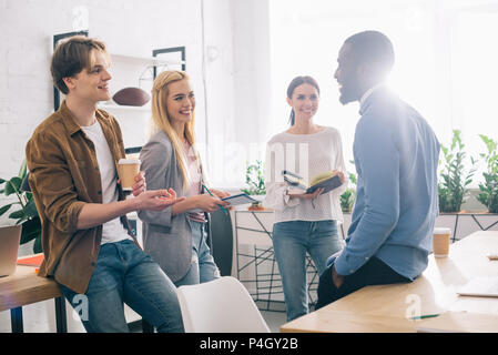 Multikulturelle Geschäftsleute mit Kaffee und Lehrbücher in Treffen im modernen Büro Stockfoto