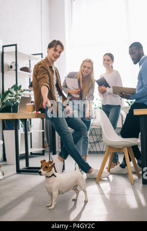 Lächelnd multiethnischen Kollegen mit Lehrbüchern und Jack Russel Terrier an der Leine in modernen Büro Stockfoto