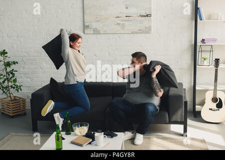 Freund und Freundin kämpfen mit Kissen im Wohnzimmer Stockfoto