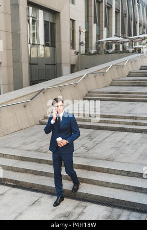 Hübscher junger Geschäftsmann im eleganten Anzug mit Kaffee trinken gehen Gespräch per Telefon, während Sie gehen, Treppen Stockfoto