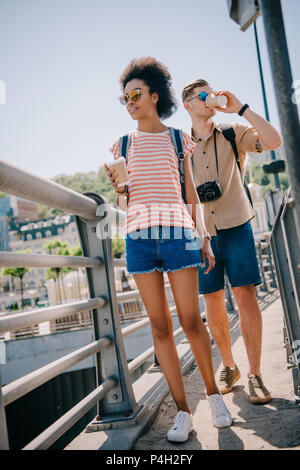 Interracial Paare der Touristen mit Einweg Tassen Kaffee und Kamera zu fuß auf die brücke Stockfoto