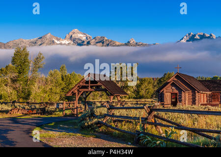 Grand Teton Bergkette und den bischöflichen Kapelle der Verklärung bei Sonnenaufgang, am frühen Morgen Licht getaucht mit Nebel und tiefliegenden Wolken. Stockfoto