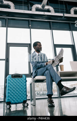 Im mittleren Alter Afrikanische amerikanische Geschäftsmann lesen Zeitung im Flughafen Stockfoto