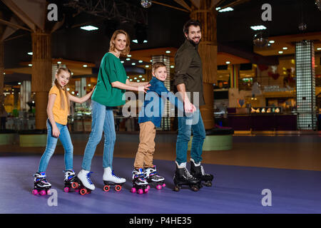 Eltern und Kinder gemeinsam Schlittschuhlaufen auf Roller Rink Stockfoto