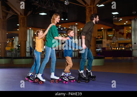 Eltern und Kinder gemeinsam Schlittschuhlaufen auf Roller Rink Stockfoto