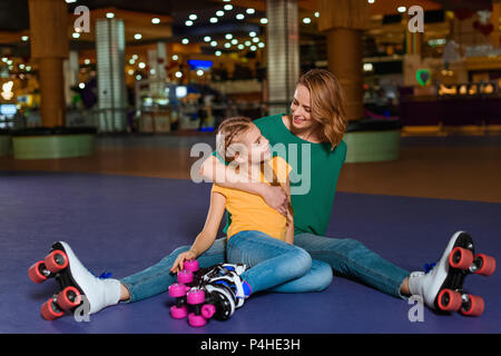 Lächelnde Mutter und Tochter sitzen auf Roller Rink zusammen Stockfoto