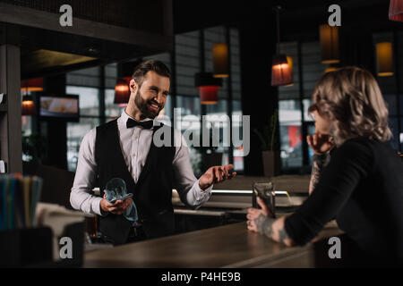 Lächelnd Barkeeper Reinigung von Glas und im Gespräch mit weiblichen Besucher Stockfoto