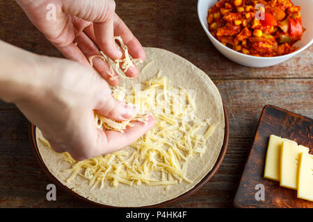 Eine Frau besprüht ein Käse Kuchen für quesadilla Tortilla. Herstellung quesadilla zu Hause. Mexikanisches Essen Stockfoto