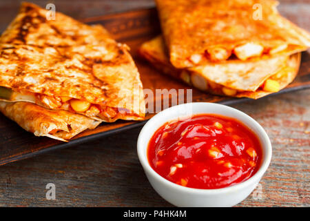 Zwei Stücke von quesadilla auf einer Platte und Sauce von Salsa auf einer hölzernen Hintergrund. Nationale mexikanische Küche, Fast Food. Stockfoto