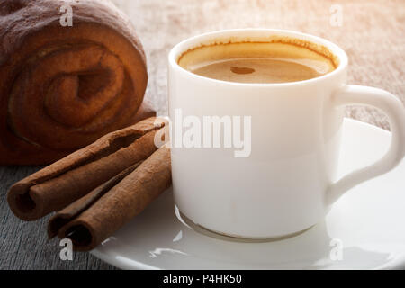 Eine Tasse duftenden Kaffee auf einem weissen Teller, Kuchen und Zimtstangen auf einer hölzernen Hintergrund. Stockfoto