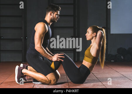 Männliche Trainer helfen jungen Sportlerin abs in der Sporthalle zu tun Stockfoto