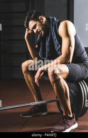 Frustrierte junge Sportler sitzen auf Barbell in der Turnhalle Stockfoto