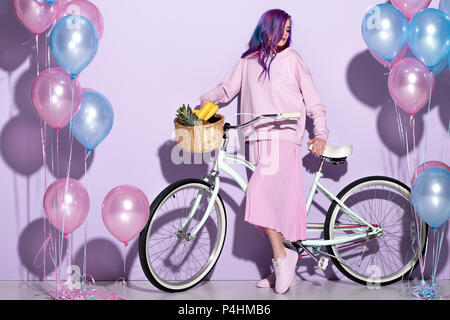 Schöne junge Frau in rosa Kleidung auf dem Fahrrad mit Ananas und Bananen im Korb Stockfoto