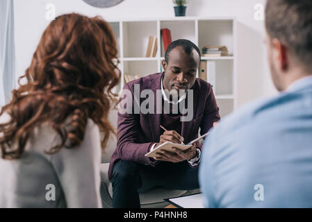 Afrikanische amerikanische Psychiater schreiben im Lehrbuch und scheidene Paare im Büro Stockfoto