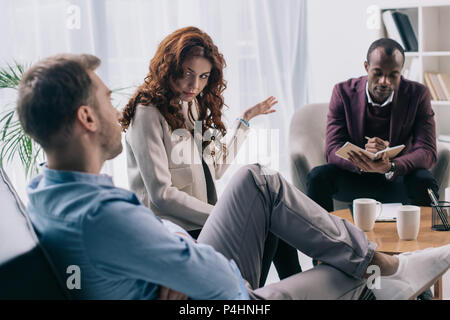 Psychiater in Lehrbuch während scheidene Paare streiten im Büro Stockfoto