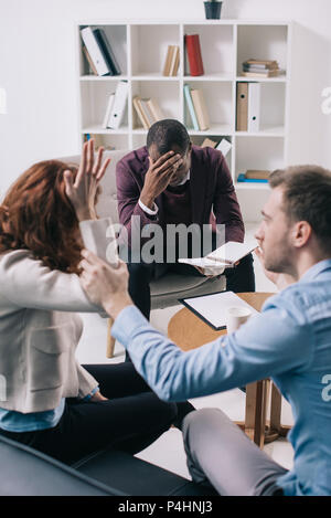 Afrikanische amerikanische Psychiater mit Lehrbuch und scheidene Paare im Büro frustriert Stockfoto