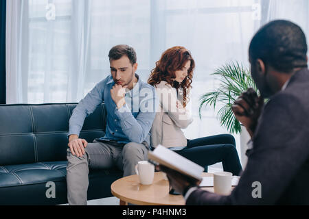 Scheiden Paar zurück sitzen auf dem Sofa und afrikanische amerikanische Ratgeber mit Lehrbuch zurück Stockfoto