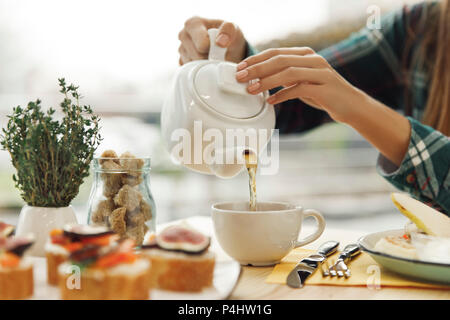 Close-up Teilweise mit Blick auf die Frau gießen Tee von Teekanne beim Frühstück Stockfoto