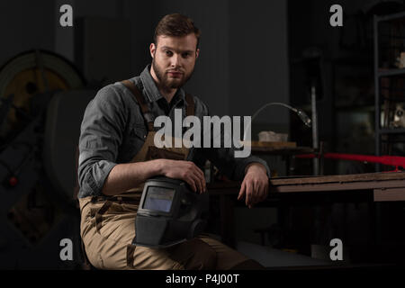 Portrait von jungen männlichen Arbeiter in Uniform holding Schutzmaske im Werk Stockfoto
