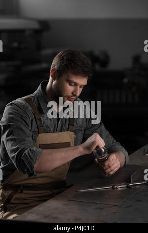 Junge männliche Arbeiter am Tisch sitzen und Öffnen der Flasche Wasser im Werk Stockfoto