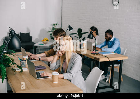 Multikulturellen Mitarbeitern am Tisch sitzen und arbeiten auf Laptops in modernen Büro Stockfoto