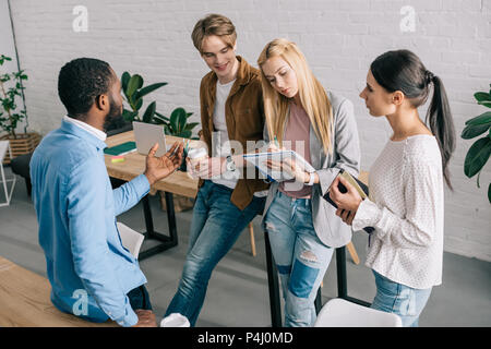 Multiethnischen Geschäftsleute mit Kaffee und Lehrbücher in Diskussion in modernen Büro Stockfoto