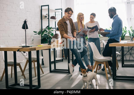 Lächelnd multikulturellen Geschäftsleute mit Jack Russel Terrier an der Leine und Lehrbücher in Diskussion in modernen Büro Stockfoto