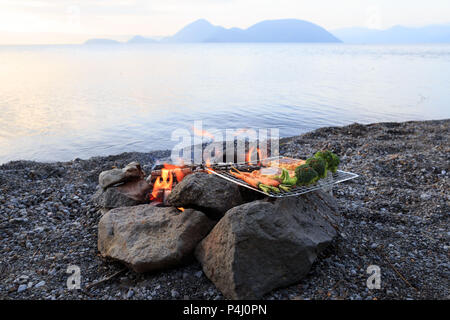 Kochen Gemüse und Tofu über offener Flamme am Strand bei Sonnenuntergang Stockfoto