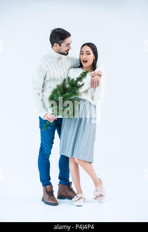 Mann überraschend asiatischen Freundin mit Weihnachtsbaum isoliert auf Grau Stockfoto