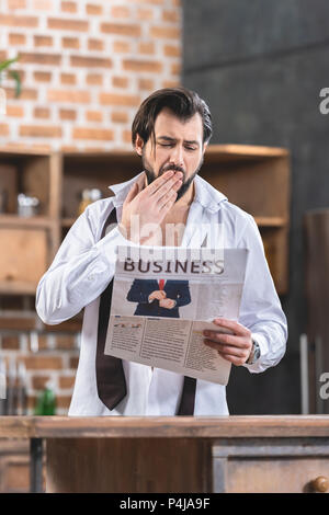 Stattliche Einzelgänger Geschäftsmann lesen Zeitung und Gähnen in Küche Stockfoto