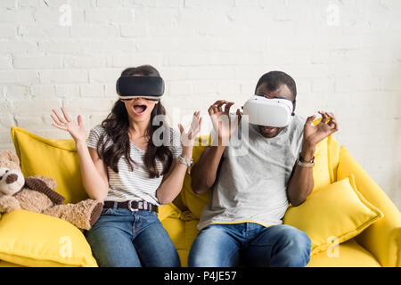 Erschrocken afrikanische amerikanische Paar in der virtuellen Realität Headsets sitzen auf der Couch Stockfoto