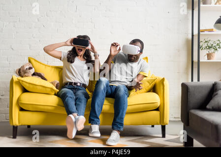 Erschrocken afrikanische amerikanische Paar in der virtuellen Realität Headsets sitzen auf der Couch Stockfoto