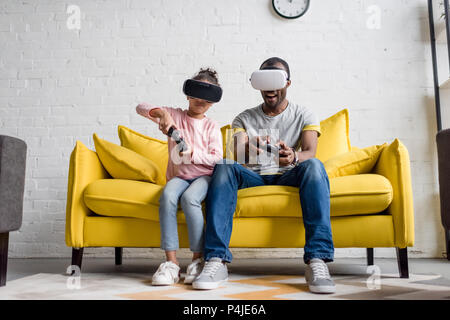 Vater und Tochter im VR-Headsets spielen Videospiele auf der Couch zu Hause Stockfoto