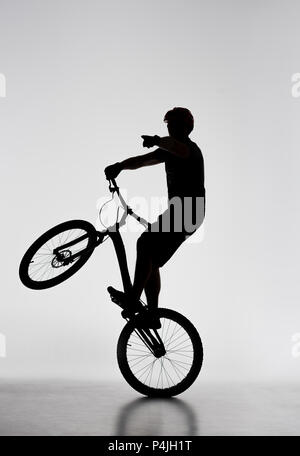 Silhouette des Versuches biker Stehen auf der Rückseite der Rad- und irgendwo hin auf Weiß Stockfoto