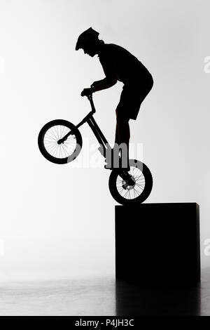 Silhouette des Versuches biker Durchführung stunt beim Balancieren auf Cube auf Weiß Stockfoto