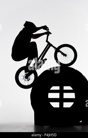 Silhouette des Versuches biker Springen am Rad des Traktors auf Weiß Stockfoto