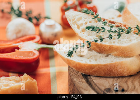 Nahaufnahme von frisch geschnittenem Baguette auf Holz Schneidebrett und Parmesan Käse mit Paprika und Champignons auf Tisch Stockfoto